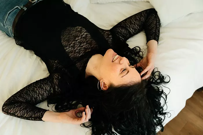 Femme allongée sur un lit, souriante et détendue, créant une ambiance accueillante posant pour les rencontres en ligne
