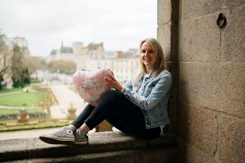 jeune femme assise sous une arcade au jardin de saint-georges à rennes lors d'un evjf tenant un ballon en coeur rose